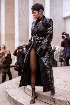 a woman in black and leopard print coat standing on steps with her legs slited