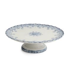 a blue and white plate on a pedestal with an ornate design in the center, against a white background