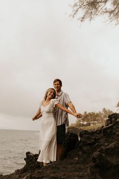 a man and woman standing on the rocks by the ocean holding each other's hands