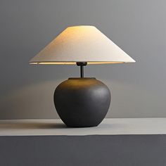 a lamp sitting on top of a table next to a gray wall with a white shade