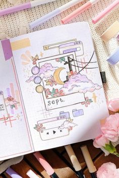 an open notebook sitting on top of a wooden table next to pink flowers and writing utensils