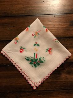 a white napkin with holly and candles on it sitting on top of a wooden table