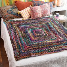 a crocheted blanket on top of a bed next to pillows and a lamp