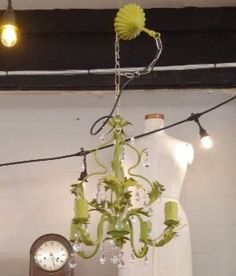 a green chandelier hanging from the ceiling next to a white dress on a mannequin