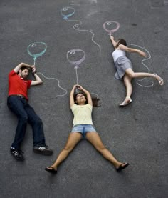 three people laying on the ground with chalk drawings in front of them and one person drawing balloons