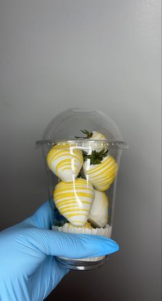 a person in blue gloves holds up a container with yellow and white striped desserts