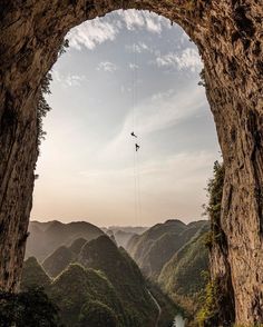 a man is suspended from the side of a cliff by a rope over a river