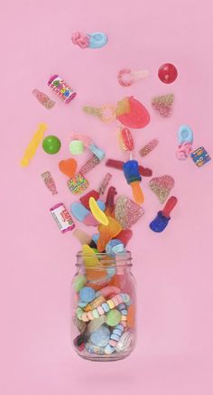 a jar filled with lots of candy on top of a pink surface