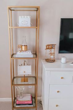 a white dresser and gold shelving unit in a room with a tv on the wall