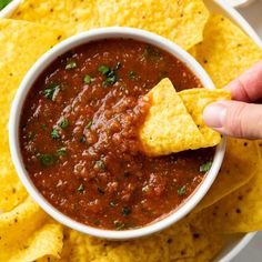 a hand dipping tortilla chips into a bowl of salsa