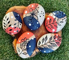 four painted rocks sitting on top of a wooden board in the grass with leaves and dots