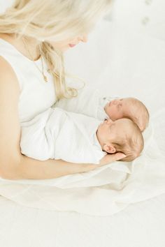 a woman holding a baby in her arms on a bed with white sheets and pillows