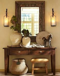 a wooden table topped with two vases next to a wall mounted mirror and stool