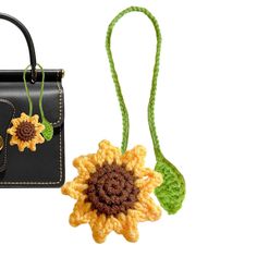 a crocheted sunflower sits next to a black purse on a white background