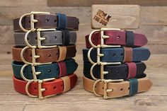 several different colored leather belts stacked on top of each other in front of a wooden box