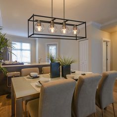 a dining room table and chairs with lights hanging over it in front of a kitchen