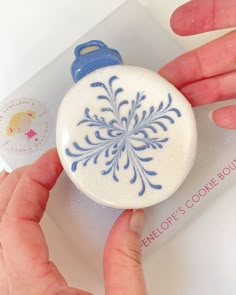 a person holding a cookie in front of a white and blue snowflake ornament