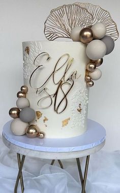 a white and gold wedding cake with the initials on it sitting on a small table