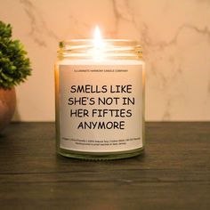 a candle that reads smells like she's not in her fiftiess anymore next to a potted plant