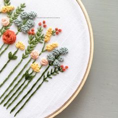 a close up of a embroidery on a hoop with flowers in the middle and green stems