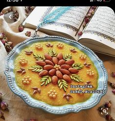 an open book on a table next to a plate with almonds and flowers in it