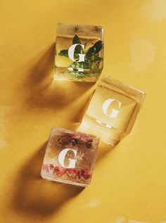 two ice cubes sitting on top of a yellow table with the letter g in them