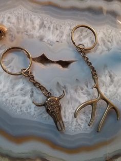 two metal scissors with horns hanging from them on a marble slabd surface, next to a pair of gold - plated hooks