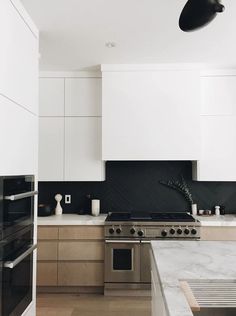 a kitchen with white cabinets and black backsplash, marble counter tops and stainless steel appliances