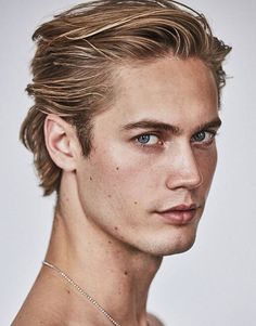 a young man with blue eyes is posing for the camera, wearing a necklace and no shirt