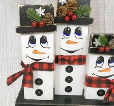 three snowmen made out of wooden blocks with pine cones on top