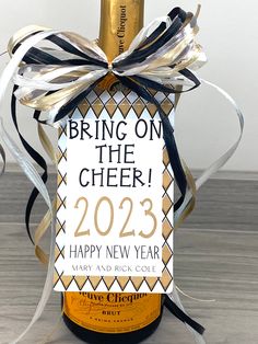 a bottle of wine is wrapped in black and white ribbon with a tag that says bring on the cheer happy new year