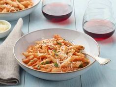 two bowls filled with pasta and garnished with parmesan cheese next to glasses of red wine