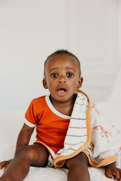 a small child sitting on top of a bed with a blanket around his neck and eyes wide open