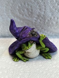 a frog with a purple hat on it's head sitting on a white surface