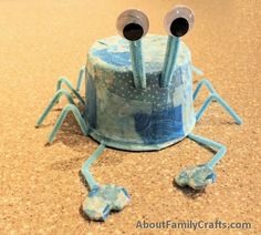 a blue cake with two eyes and legs on the top, sitting on a table