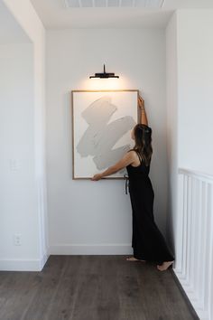 a woman standing in front of a white wall with a painting hanging on the wall