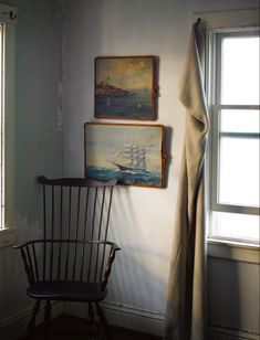 two paintings hang on the wall next to a rocking chair in front of a window