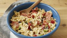 a blue bowl filled with pasta and meat on top of a wooden table next to a napkin