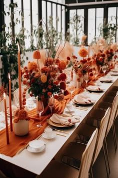 a long table with orange flowers and candles on it is set for an elegant dinner