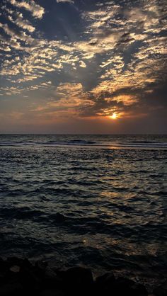 the sun is setting over the ocean with clouds in the sky and water below it