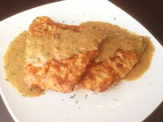 two pieces of fried chicken covered in gravy on a white plate with sauce