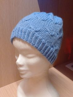 a white mannequin head wearing a blue knitted hat on top of a wooden table