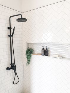 the shower head is mounted on the wall next to the shelf with soap bottles and a potted plant