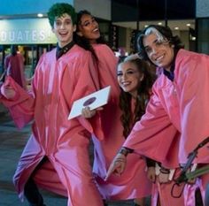 group of people in pink graduation gowns posing for the camera with one holding a piece of paper