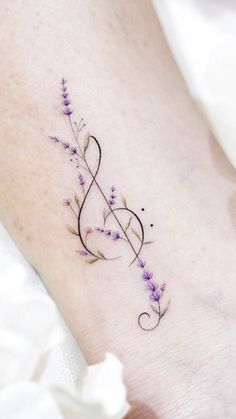 a small tattoo on the ankle with purple flowers and an treble in the middle