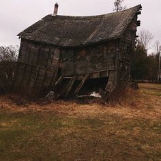 an old wooden barn sitting on top of a grass covered field