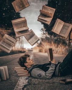 a man laying on top of a wooden bench next to books flying in the air