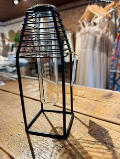 a glass vase sitting on top of a wooden table in front of clothes hanging up