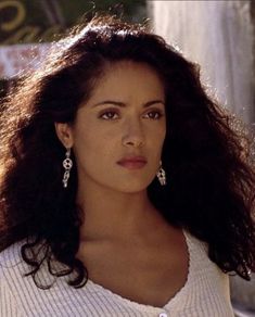 a close up of a person with long hair and wearing white shirt, earrings and sweater