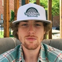 a man wearing a flanness hat sitting on a couch in front of a building